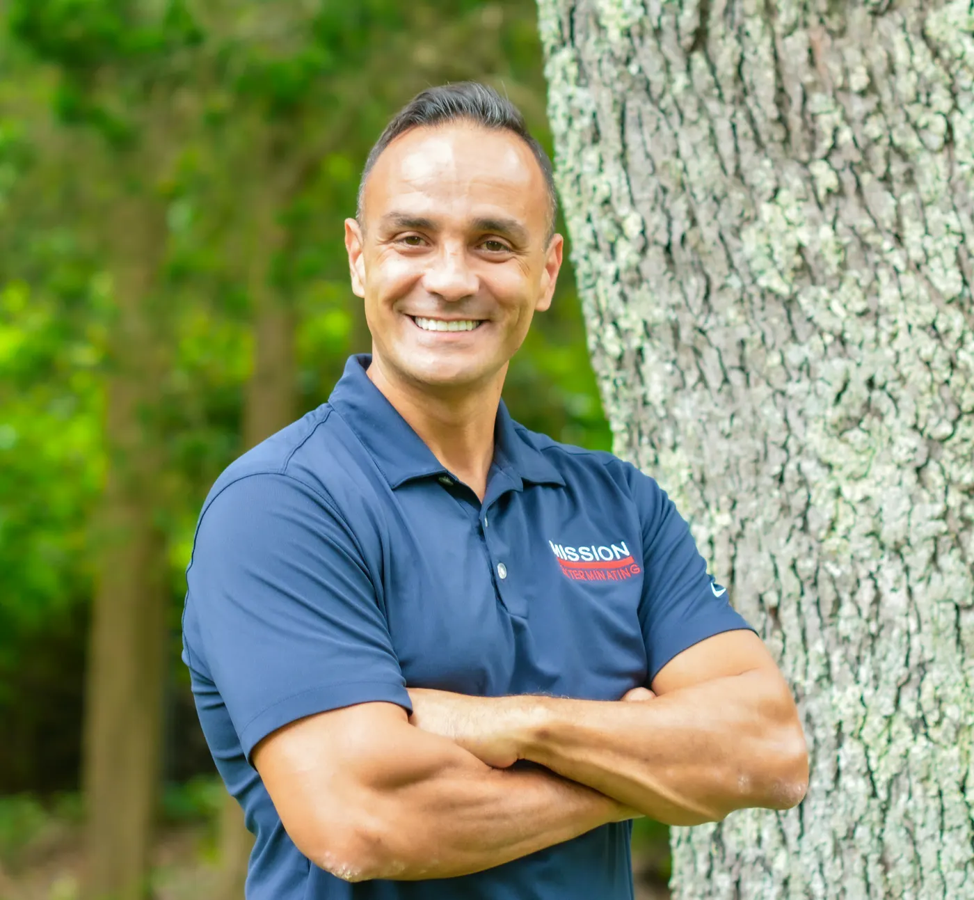 Frank in the navy Mission polo, arms crossed, standing by a tree